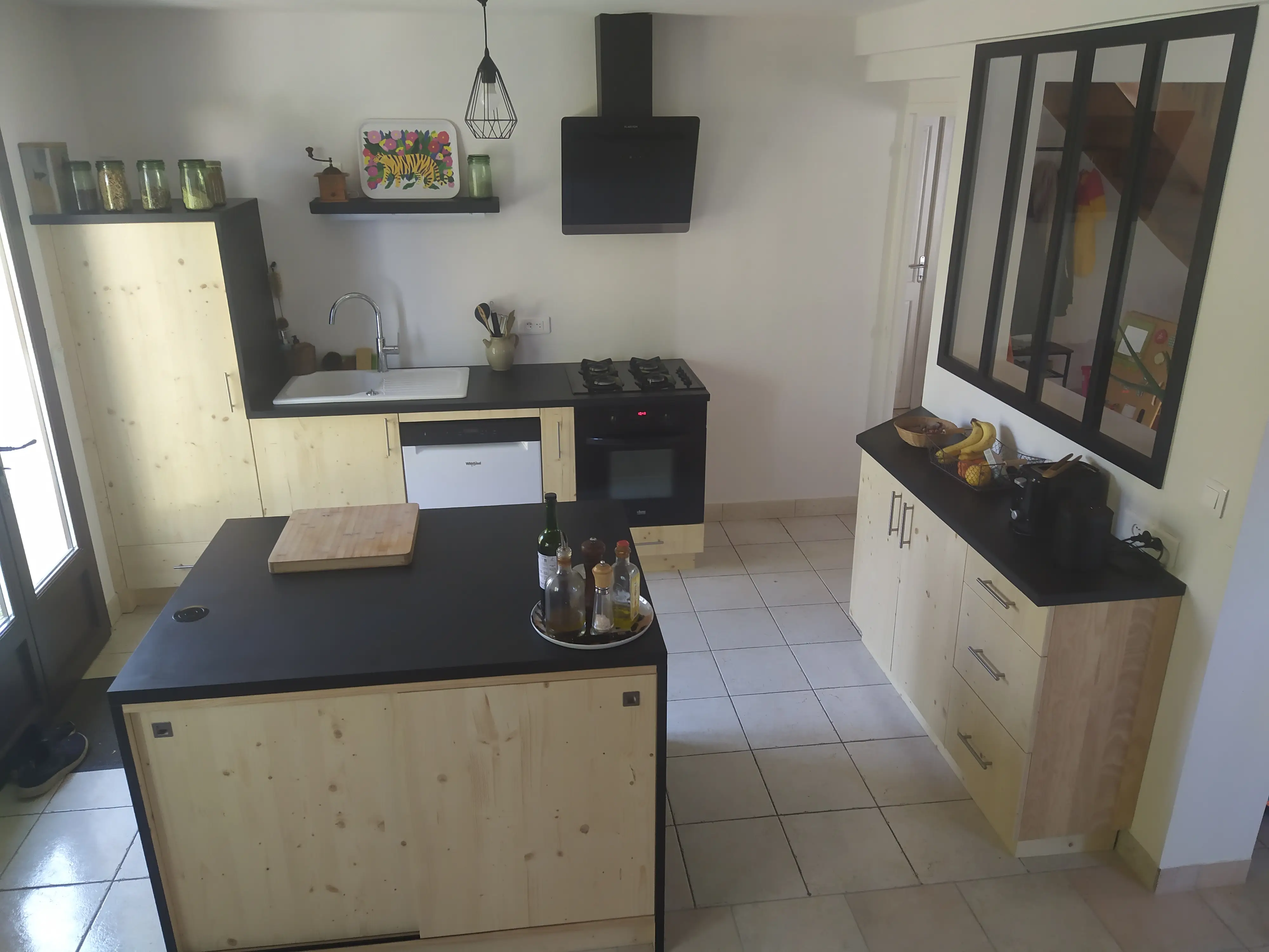 Cuisine moderne en bois clair avec un îlot central noir, des planchers de travail noirs, une hotte aspirante et une verrière d'intérieur.