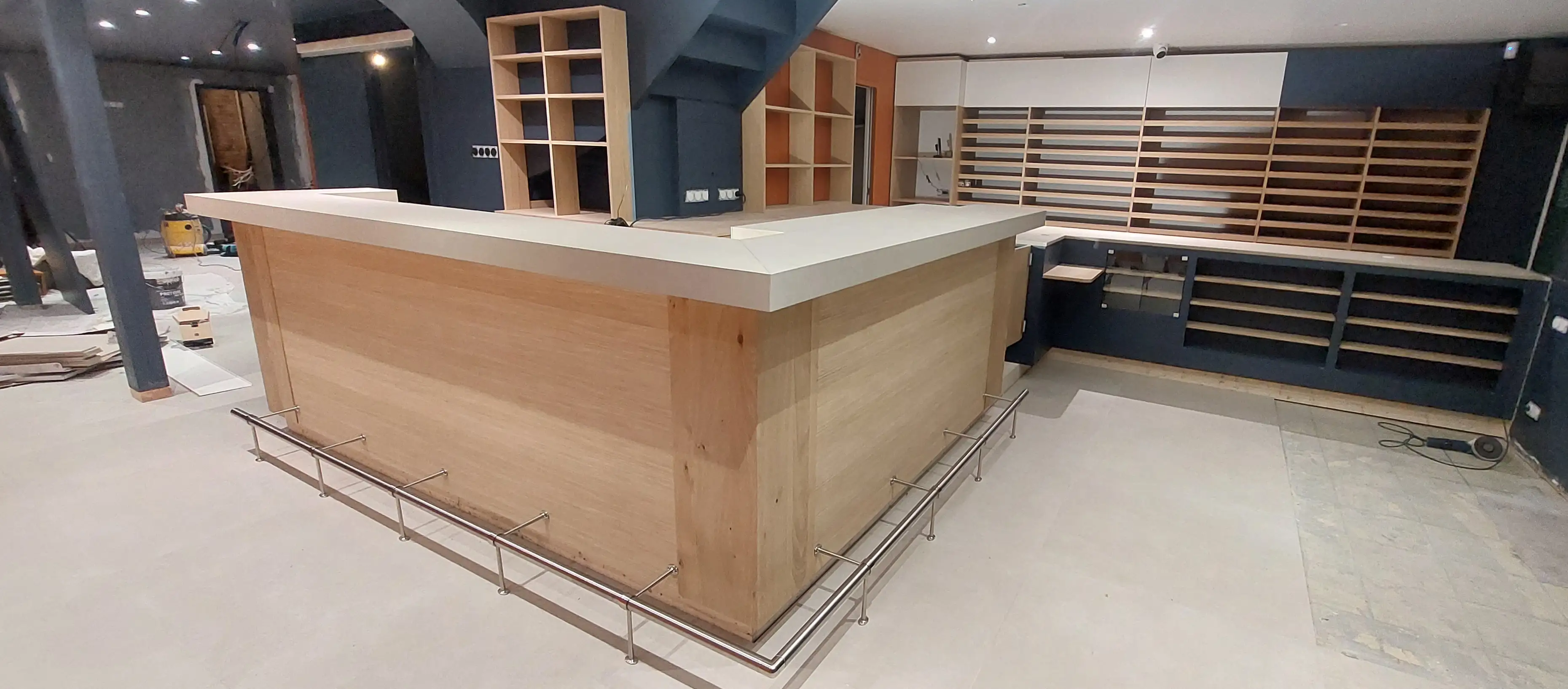 Grand comptoir d'accueil ou bar sur mesure en bois clair installé dans un espace commercial en cours d'aménagement.