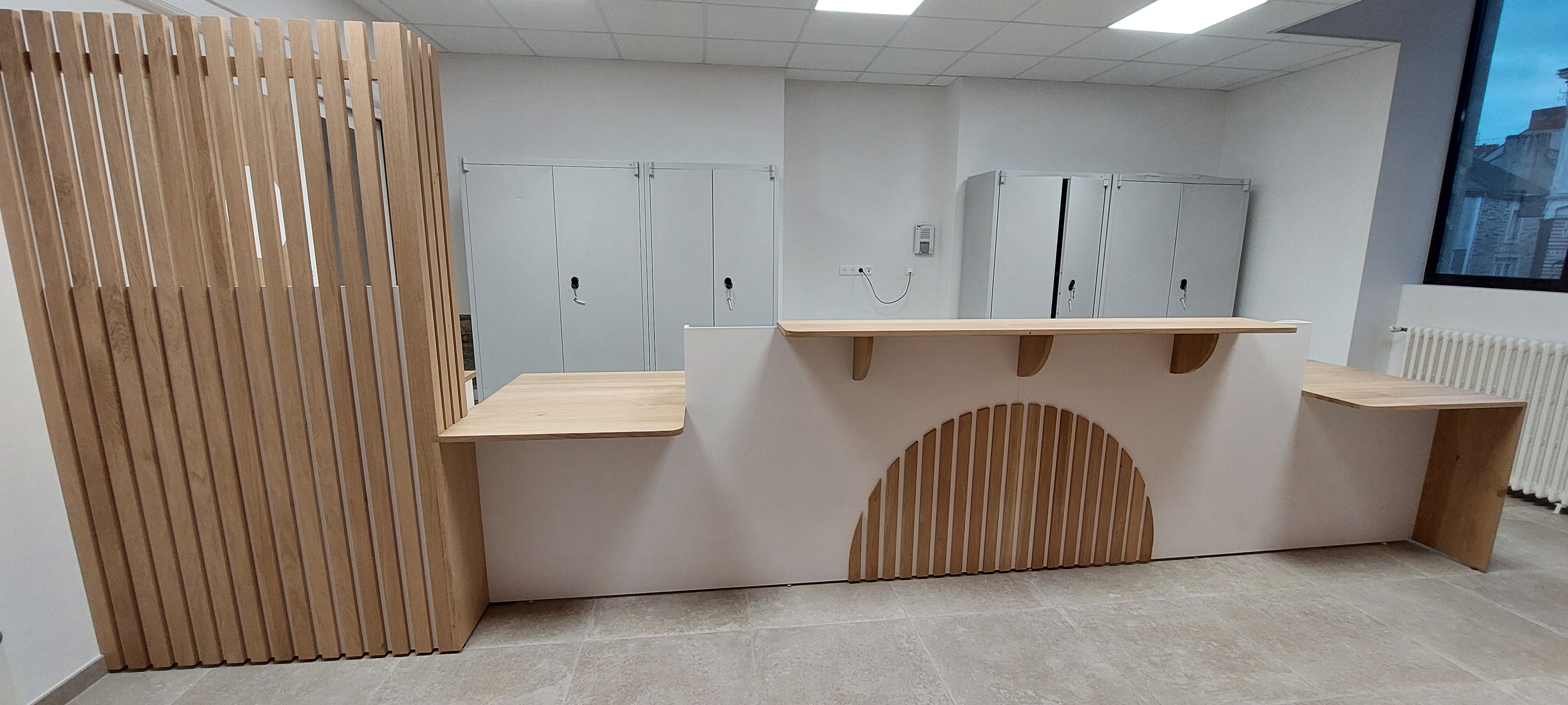 Vue de face d'un comptoir de caisse ou d'accueil blanc et bois clair, décoré de tasseaux de bois verticaux formant un arc de cercle.
