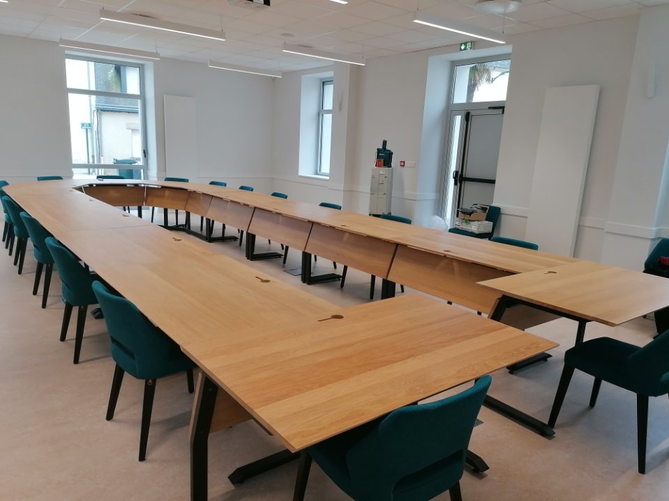 Grande table de conférence en bois clair installée en U, entourée de chaises de bureau vert canard dans une salle d'entreprise.